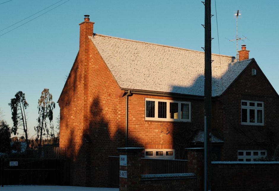 A brick house with a snow-dusted roof under morning sunlight, depicting a quiet winter scene.
